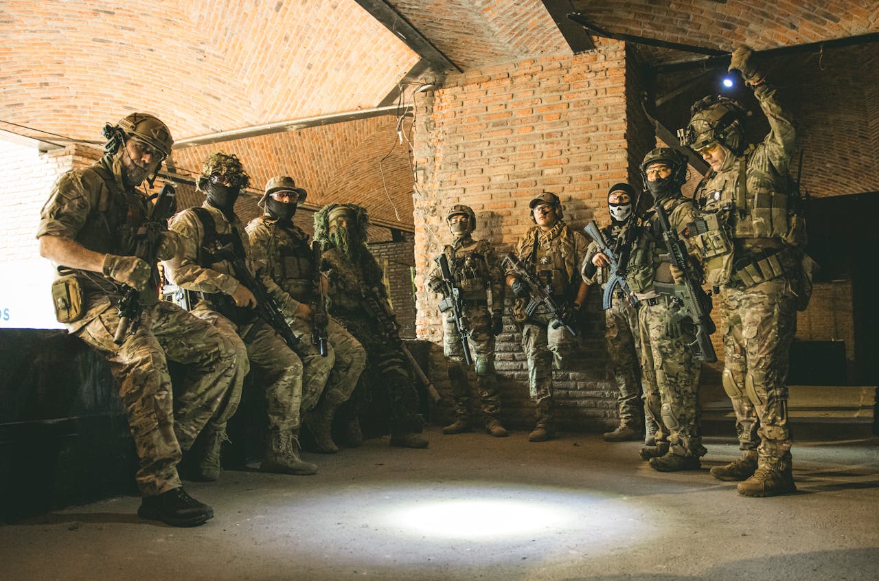 Soldiers in tactical gear gather in a brick underground tunnel with dim lighting.